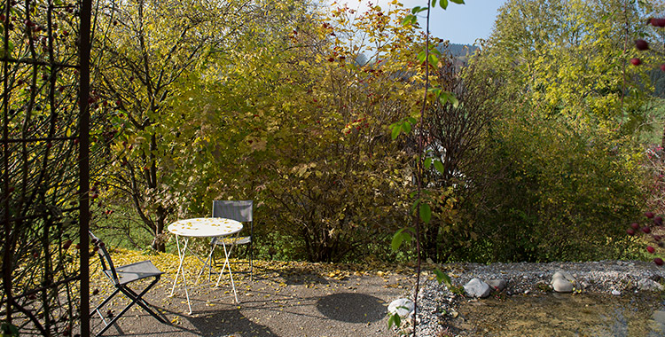 Kleines, weisses Tischchen und Faltstühle vor Wildsträucherhecke